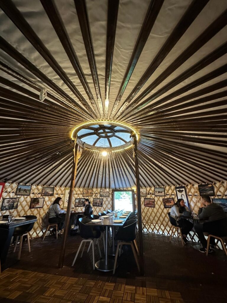 Interior of Naadam yurt showing Mongolian photos and traditional decor, tables for two and large group seating
