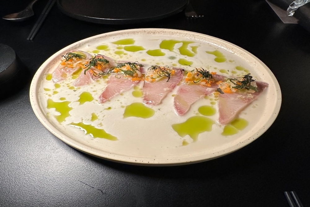 Kingfish Crudo with green mango and coconut sauce in a white bowl.