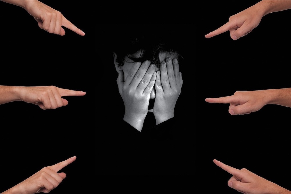 Black and white illustration of a person covering their face with hands while surrounded by finger-pointing figures, symbolizing online bullying and social isolation, related to Second Sister by Chan Ho-Kei
